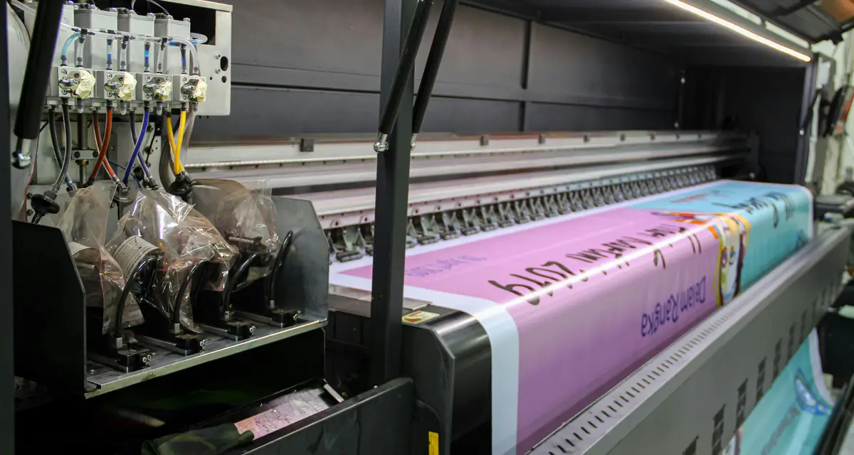 A wide-format printer printing a vivid pink and blue design onto a long roll of transfer paper